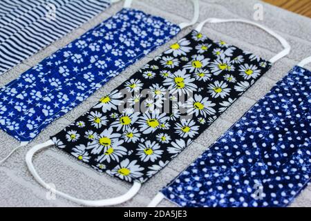 Close up view of four various print hand-washed COVID protective face masks, drying on a cotton towel on kitchen table Stock Photo
