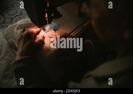 Close - up of old hand of a senior caucasian woman on a sewing machine with a lamp Stock Photo