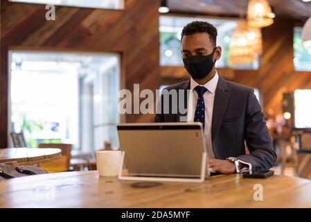 Businessman using laptop while wearing protective facial mask in coffee shop Stock Photo