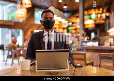 Businessman using laptop while wearing protective facial mask in coffee shop Stock Photo
