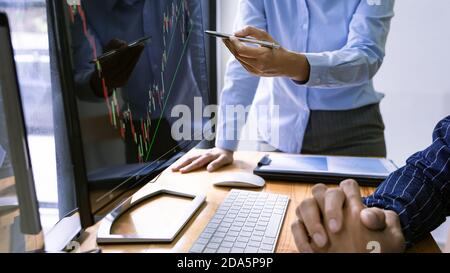 broker showing some ascending to his colleague planning and analyzing graph stock market trading with stock chart data on multiple computer screens Stock Photo