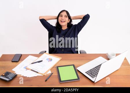 An attractive and cheerful young business woman is stretching and smiling as she sits up. On modern office desk Stock Photo