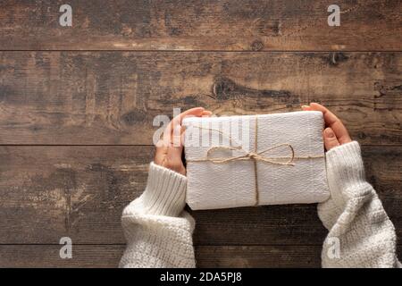 woman holding christmas gift box. Wooden rustic table. Top view woman hands holding present box. Female hand holding gift box on wood table background Stock Photo