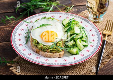 Healthy breakfast. Christmas brunch. Avocado sandwich with fried egg and cucumber with arugula on wooden table. Stock Photo