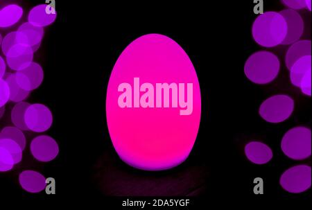 Shining Hot Pink Egg Shaped Table Lamp with Purple Bokeh Light on Dark Background Stock Photo