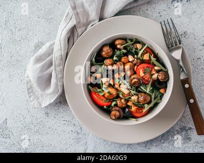 Salad with arugula, mini champignons, cherry tomatoes, black olives, pine nuts. Vegetarian salad top view or flat lay. Copy space. Horizontal Stock Photo