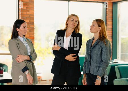Three business women discussing dry topics in a cafe. Team building concept. Photo against the background of large windows. Stock Photo