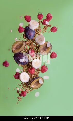 Falling granola, raspberry, plum, banana on a green background. Food levitation Stock Photo