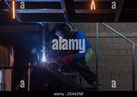 Industrial worker at a welding plant. A man dressed in protective suits and a mask welds a metal structure. Construction and manufacturing concept Stock Photo