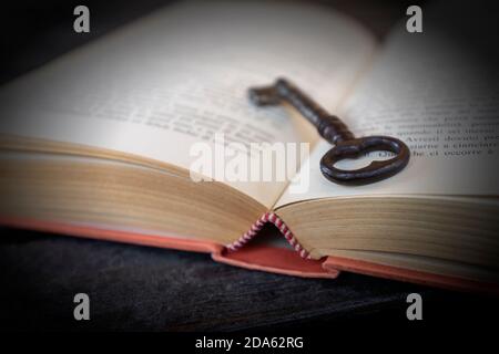 An old key is leaning inside an old book against a black background Stock Photo