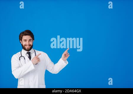 Horizontal banner of smiling young male doctor showing and presenting something with hand, isolated on blue background with copy space on the left Stock Photo