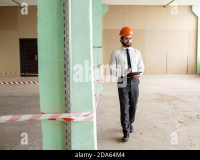 A young bearded Architect in a construction helmet on a construction site checks the result Stock Photo