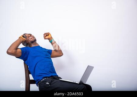 young african man feeling excited and positive while making a phone call, also has a laptop on his lap Stock Photo