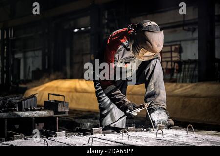 A young  man welder in  uniform, welding mask and welders leathers, weld  metal  with a  welding machine at the construction site, white smoke Stock Photo