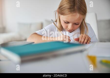 Thoughtful small miss writing letter at the table in room inside Stock Photo