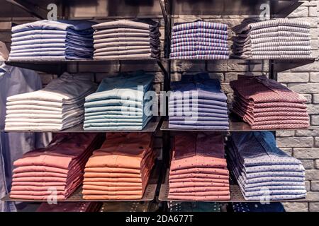 Clothes displayed in store, men's shirts shirts of different colors on the shelf, beautifully and neatly arranged in piles Stock Photo