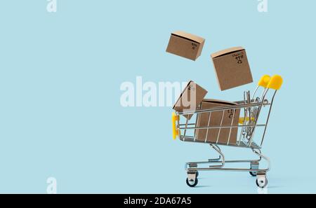 Toy shopping cart with boxes in air on blue background. Copy space for text or design. Sale, discount, shopping and delivery concept. Consumer society Stock Photo