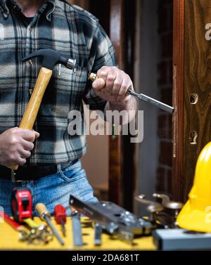 Close-up. Carpenter with hammer and chisel prepares the hole for the lock of a wooden door. Construction industry. Stock Photo