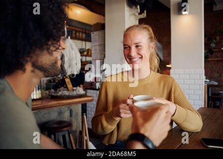 Portrait of beautiful young woman holding coffee mug and talking to man with curly hair in modern cafe Stock Photo