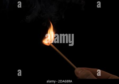 Hand holding a lighted match with fire flame and smoke on a black background. Stock Photo