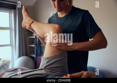 Closeup of young woman physiotherapist giving therapy treatment to patient on leg Stock Photo
