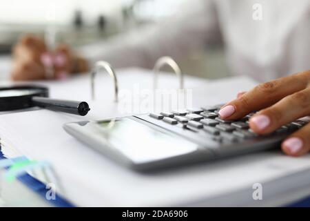 Women's hands on calculator next to magnifying glass and documents Stock Photo