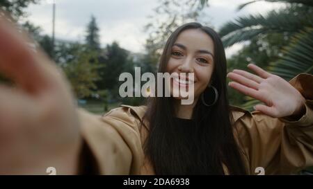 Charming young smiling face woman holding camera or phone in hand and she makes video call or she is recording video for her fans, video call and vlog Stock Photo