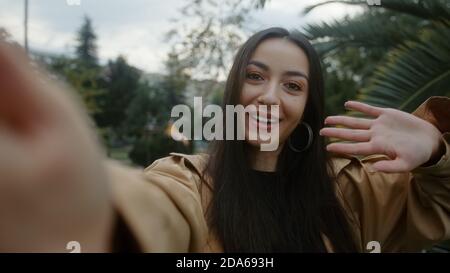 Charming young smiling face woman holding camera or phone in hand and she makes video call or she is recording video for her fans, video call and vlog Stock Photo