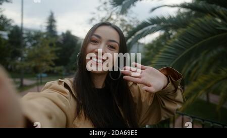 Pretty smiling face woman, holding camera or phone in hand and she is waving to the camera and she pointing out and she makes video call or she is rec Stock Photo