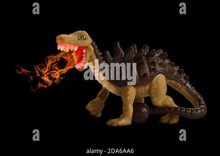 Fire breathing toy dinosaur. Children's toy, plastic animal figure isolated on black background, fantasy composite. Dinosaur with spikes and tail club Stock Photo