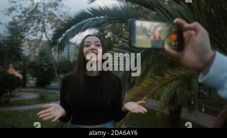 Young beautiful smiling fashion blogger woman making online new video blog, vlog, with her smartphone on nature background. Influencer speaking to cam Stock Photo