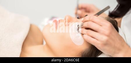 Young caucasian woman having eyelash extension procedure in beauty salon. Beautician glues eyelashes with tweezers Stock Photo