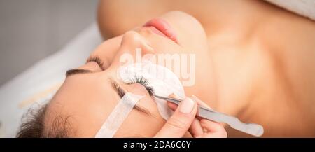 Young caucasian woman having eyelash extension procedure in beauty salon. Beautician glues eyelashes with tweezers Stock Photo