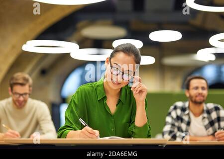 Never stop learning. Focused asian woman wearing eyeglasses making some notes while studying with colleagues during corporate training or seminar. Business education concept Stock Photo