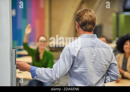 Rear view of a male coach or speaker pointing at giving a presentation to audience during corporate seminar or training, selective focus. Business education concept Stock Photo