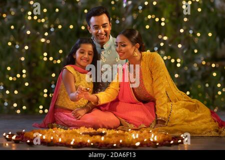 Parents with their daughter placing diyas together Stock Photo