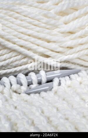knitting yarn lies next to ball, color is white, thread has soft structure, knitting needles large and gray; flat lay, close up Stock Photo