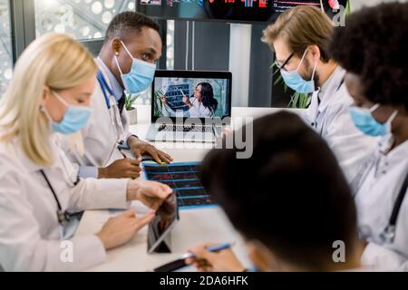 Medical and healthcare concept. Team of multiethnic diverse doctors scientists, wearing face masks, at online webinar with young experienced Afican Stock Photo