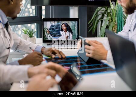 Cropped image of multiracial doctors using laptop for video conference with African female colleague, discussing CT scan results and making notes on Stock Photo