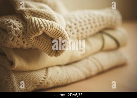 A neat stack of white warm wool sweaters, with the sleeve of one of them hanging down from the top, illuminated by the light. Clothing for cold weathe Stock Photo