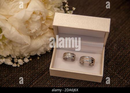 Wedding rings in a box next to a bouquet made of white roses Stock Photo