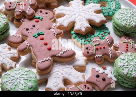 Plate of decorated Christmas gingerbread men and cookies with snowflakes and wreaths and macarons Stock Photo