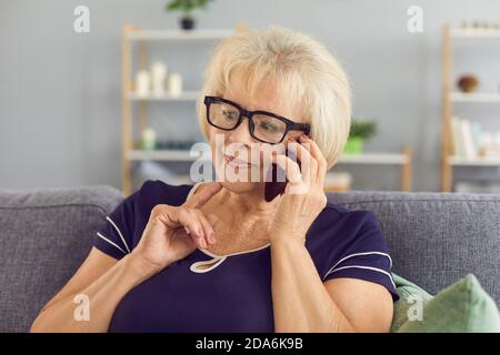 Pensive mature woman talking to relatives on mobile phone sitting on couch at home Stock Photo