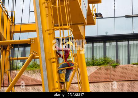 Indian operator is climbing up the vertical staircase on a gantry crane for construction work at urban area. Singapore, 2020. Stock Photo