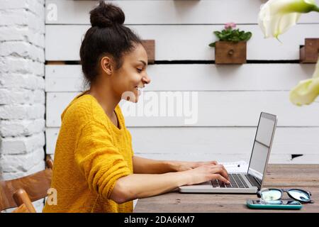 Side view portrait of young african american woman working on laptop at cafe Stock Photo