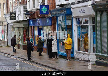 Rye, East Sussex, UK. 10 Nov, 2020. UK Weather: With the town of Rye in East Sussex relying on visitors for the economy of the town, few people walk the streets on a rainy but mild day. People wearing face masks queueing in the rain at the chemist in the high street. Photo Credit: Paul Lawrenson-PAL Media/Alamy Live News Stock Photo