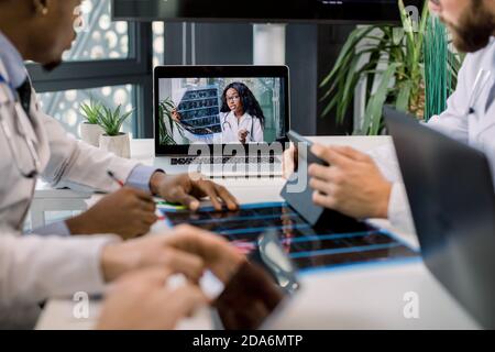 Cropped image of multiracial doctors using laptop for video conference with African female colleague, discussing CT scan results and making notes on Stock Photo