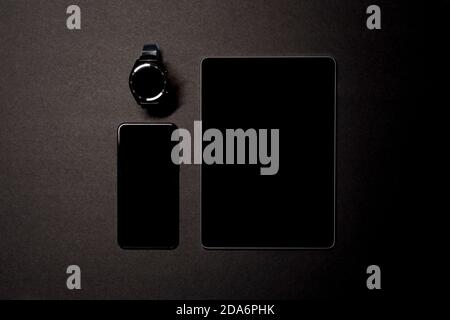 Overhead shot of a smartwatch, smartphone and a tablet on a black background. Wireless technology concept. Horizontal photography. Copyspace Stock Photo