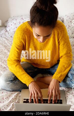 Portrait of a female student sitting on bed and working on laptop Stock Photo