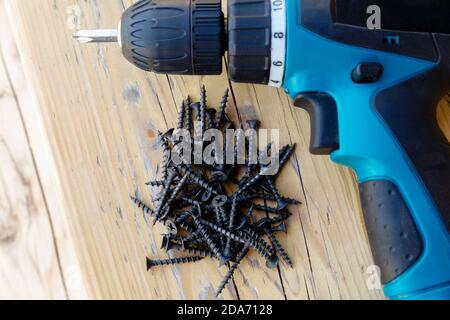 The concept of repair and construction of wooden structures and fasteners with screws. In the frame, a screwdriver and a group of black screws on a wooden surface. Stock Photo